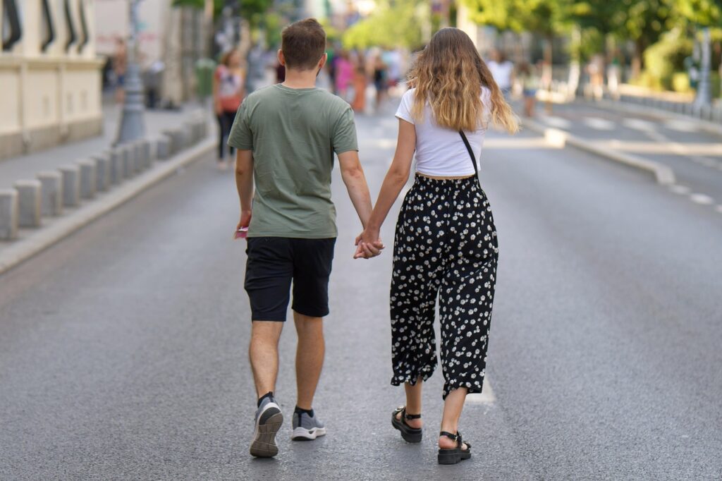Fiatal pár kézen fogva sétál egy utcán, hátulról fényképezve, arcuk nem látszik
